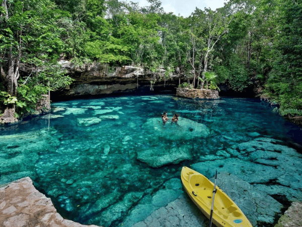 A yellow kayak floats on blue water by a cenote